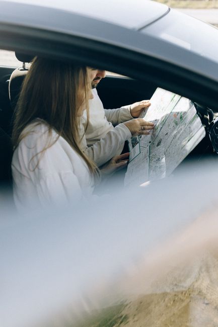 A woman sitting inside a car holding a floral arrangement or bouquet, with the car window framing her in the foreground. The bouquet features a vibrant mix of fresh flowers, including pink and yellow 